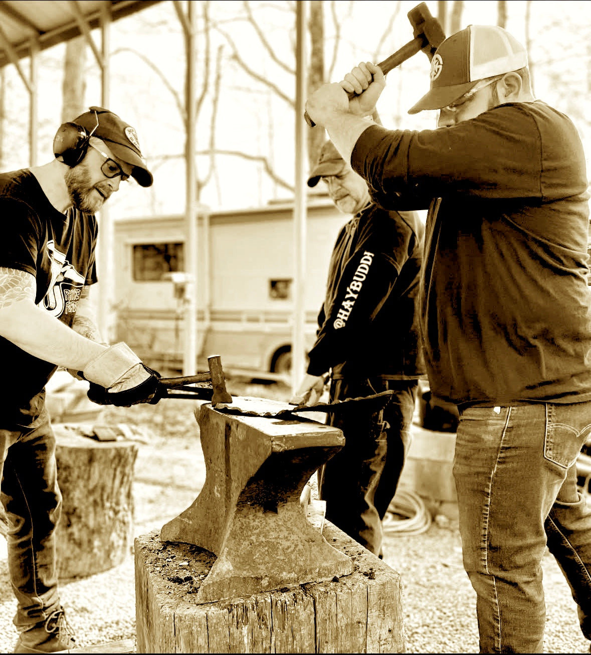 Three men working together on an anvil outdoors.